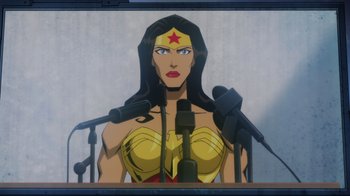 Movie still from “Injustice” (2021), directed by Matt Peters – A woman with a red star on her head is standing behind microphones; Medium shot, Low angle