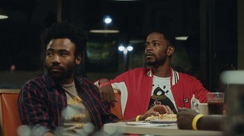 Movie still from “Atlanta” (2016), created by Donald Glover – Two men are sitting at a table with food in front of them; Medium shot, Over the shoulder angle