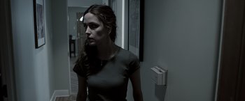 Movie still from “Insidious” (2010), directed by James Wan – A young woman standing in a dark room; Medium shot, Over the shoulder angle