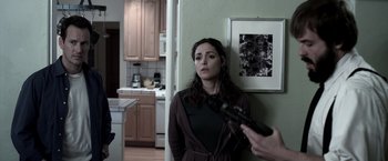 Movie still from “Insidious” (2010), directed by James Wan – A woman standing in a kitchen holding a gun; Medium shot, Over the shoulder angle