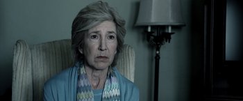 Movie still from “Insidious” (2010), directed by James Wan – An older woman sitting in a chair in front of a lamp; Close Up shot, Over the shoulder angle