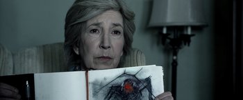 Movie still from “Insidious” (2010), directed by James Wan – An older woman holding up a drawing of a spider; Close Up shot, Over the shoulder angle