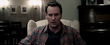 Movie still from “Insidious” (2010), directed by James Wan – A person sitting in a chair wearing a plaid shirt; Close Up shot, High angle