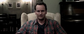 Movie still from “Insidious” (2010), directed by James Wan – A person sitting in a chair wearing a plaid shirt; Close Up shot, Over the shoulder angle