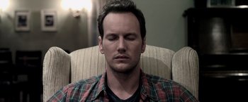 Movie still from “Insidious” (2010), directed by James Wan – A person sitting in a chair with his eyes closed; Close Up shot, High angle