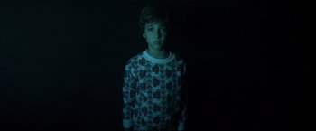 Movie still from “Insidious” (2010), directed by James Wan – A young boy is standing in a dark room; Medium shot, Low angle