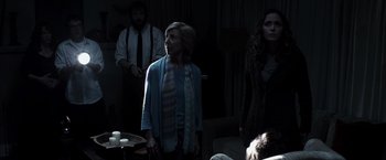 Movie still from “Insidious” (2010), directed by James Wan – A group of people standing in a dark room; Medium shot, Over the shoulder angle