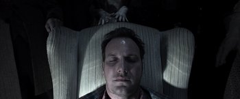 Movie still from “Insidious” (2010), directed by James Wan – A man with his eyes closed and his hands on the back of a couch; Close Up shot, Overhead angle