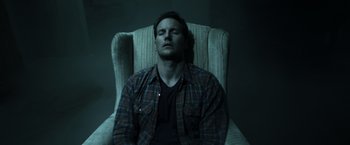 Movie still from “Insidious” (2010), directed by James Wan – A man sitting in a chair with his eyes closed; Medium shot, High angle