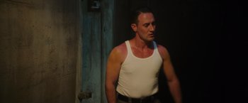Movie still from “Insidious: The Last Key” (2018), directed by Adam Robitel – A man in a white tank top standing next to a door; Medium shot, Low angle