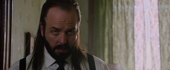 Movie still from “Insidious: The Last Key” (2018), directed by Adam Robitel – A man with long hair and a beard wearing a white shirt; Close Up shot, Over the shoulder angle