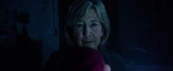 Movie still from “Insidious: The Last Key” (2018), directed by Adam Robitel – An older woman looking at the camera in a dimly - lit room; Close Up shot, Over the shoulder angle