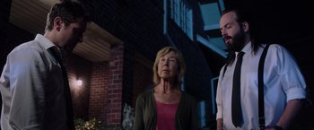 Movie still from “Insidious: The Last Key” (2018), directed by Adam Robitel – A woman standing next to a man in front of a brick building; Medium shot, Low angle