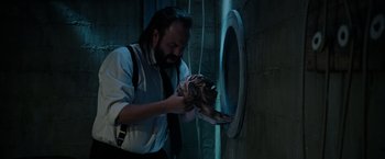 Movie still from “Insidious: The Last Key” (2018), directed by Adam Robitel – A bearded man in a suit and tie holding a fish; Medium shot, Low angle