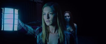 Movie still from “Insidious: The Last Key” (2018), directed by Adam Robitel – A woman standing next to another woman in a dark room; Close Up shot, Low angle