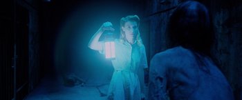 Movie still from “Insidious: The Last Key” (2018), directed by Adam Robitel – A woman holding a lantern in a dark room; Medium shot, Over the shoulder angle