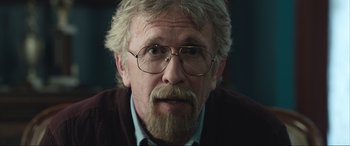 Movie still from “Insidious: The Red Door” (2023), directed by Patrick Wilson – An older man with a beard wearing glasses and a sweater; Close Up shot, Over the shoulder angle