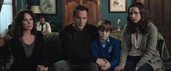 Movie still from “Insidious: The Red Door” (2023), directed by Patrick Wilson – A man and a boy sitting on a couch together; Medium shot, Over the shoulder angle