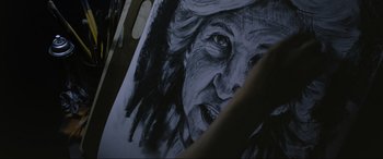 Movie still from “Insidious: The Red Door” (2023), directed by Patrick Wilson – An old woman's face drawn in black and white on a piece of paper; Extreme Close Up shot, Over the shoulder angle