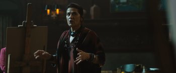 Movie still from “Insidious: The Red Door” (2023), directed by Patrick Wilson – A woman standing in front of a table with other people; Medium shot, Over the shoulder angle