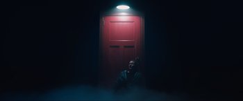 Movie still from “Insidious: The Red Door” (2023), directed by Patrick Wilson – A man standing in front of a red door in a dark room; Wide shot, Low angle