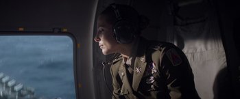 Movie still from “Interceptor” (2022), directed by Matthew Reilly – A woman in a uniform is wearing headphones and looking out a window; Medium shot, Low angle