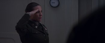 Movie still from “Interceptor” (2022), directed by Matthew Reilly – A woman in uniform saluting in front of a wall clock; Medium shot, Low angle