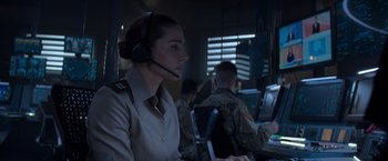 Movie still from “Interceptor” (2022), directed by Matthew Reilly – A woman wearing a headset in front of a computer; Medium shot, Low angle