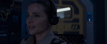 Movie still from “Interceptor” (2022), directed by Matthew Reilly – A woman wearing a pair of headphones is smiling; Close Up shot, Over the shoulder angle