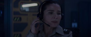 Movie still from “Interceptor” (2022), directed by Matthew Reilly – A woman wearing a headset while sitting in a room; Close Up shot, Over the shoulder angle