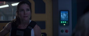 Movie still from “Interceptor” (2022), directed by Matthew Reilly – A woman standing in front of a wall with a cell phone on it; Close Up shot, Over the shoulder angle