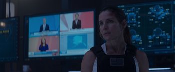 Movie still from “Interceptor” (2022), directed by Matthew Reilly – A woman in front of a television in a room; Close Up shot, Over the shoulder angle