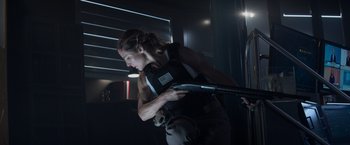 Movie still from “Interceptor” (2022), directed by Matthew Reilly – A woman holding a gun while standing next to a wall; Medium shot, Low angle