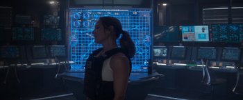 Movie still from “Interceptor” (2022), directed by Matthew Reilly – A woman standing in front of a large screen; Medium shot, Over the shoulder angle