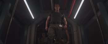 Movie still from “Interceptor” (2022), directed by Matthew Reilly – A man standing on a train with other people standing in the background; Medium shot, Low angle
