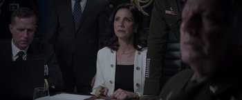 Movie still from “Interceptor” (2022), directed by Matthew Reilly – A woman sitting at a table in front of a group of people; Medium shot, Over the shoulder angle