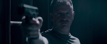 Movie still from “Interceptor” (2022), directed by Matthew Reilly – A person holding a gun in a dark room; Close Up shot, Low angle