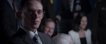 Movie still from “Interceptor” (2022), directed by Matthew Reilly – A person wearing a suit and glasses; Close Up shot, Over the shoulder angle