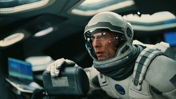 Movie still from “Interstellar” (2014), directed by Christopher Nolan – A man in a spacesuit holding a box in a car; Close Up shot, Overhead angle