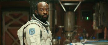 Movie still from “Interstellar” (2014), directed by Christopher Nolan – A man in a space suit standing next to a table in a room; Close Up shot, Over the shoulder angle