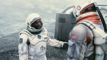 Movie still from “Interstellar” (2014), directed by Christopher Nolan – Two people in spacesuits standing next to each other on a beach; Medium shot, Over the shoulder angle