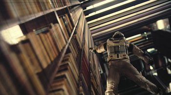 Movie still from “Interstellar” (2014), directed by Christopher Nolan – A man in a spacesuit climbing a book shelf; Wide shot, Overhead angle