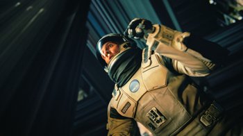 Movie still from “Interstellar” (2014), directed by Christopher Nolan – A man in a space suit holding a gun in his hand; Medium shot, Low angle