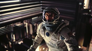 Movie still from “Interstellar” (2014), directed by Christopher Nolan – A man in a spacesuit is standing in a room; Medium shot, Overhead angle