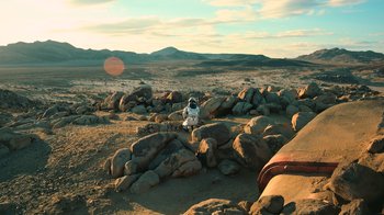 Movie still from “Interstellar” (2014), directed by Christopher Nolan – An astronaut sitting on top of a pile of rocks in the middle of the desert; Extreme Wide shot, High angle