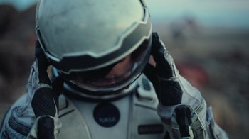 Movie still from “Interstellar” (2014), directed by Christopher Nolan – A man in a space suit is holding his helmet; Close Up shot, Low angle
