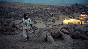 Movie still from “Interstellar” (2014), directed by Christopher Nolan – A man in a spacesuit walking across a rocky field; Wide shot, High angle