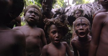 Movie still from “Into the Inferno” (2016), directed by Werner Herzog – A group of young men standing next to each other in a forest; Medium shot, High angle