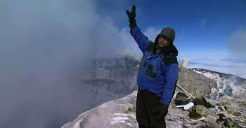 Movie still from “Into the Inferno” (2016), directed by Werner Herzog – A man standing on top of a snow covered slope; Wide shot, High angle