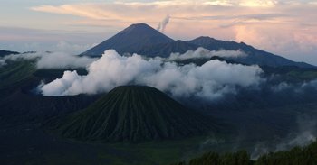 Movie still from “Into the Inferno” (2016), directed by Werner Herzog – A view of a mountain range with a cloud filled sky in the background; Extreme Wide shot, High angle